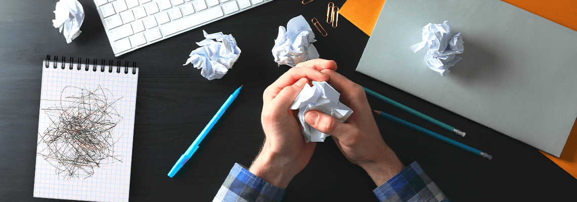 Mão sobre uma mesa amassam papéis, pontuando a possível necessidade de refação